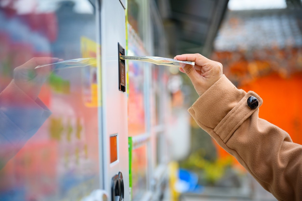 This image captures a person feeding a banknote into a traditional vending machine, a familiar scene that is becoming increasingly rare as technology evolves.
